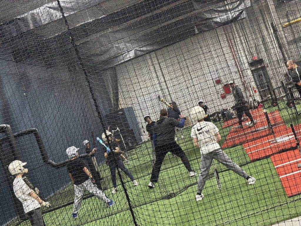 A group of youth baseball players is watching as their coach demonstrates a swing