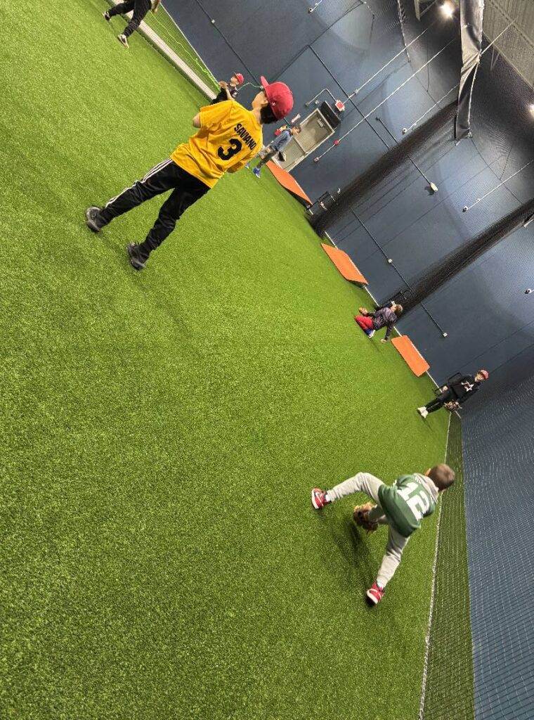 Young baseball players inside the pitching cages are working on fielding.