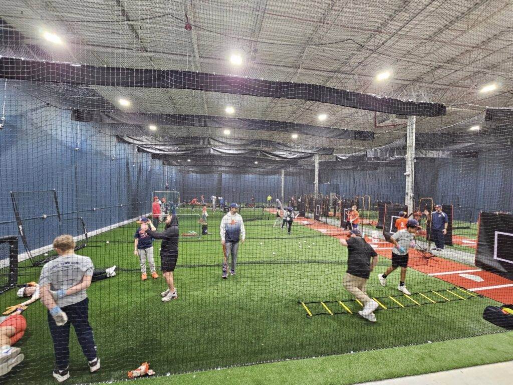 A wideshot of a group of players and coaches inside the batting cages